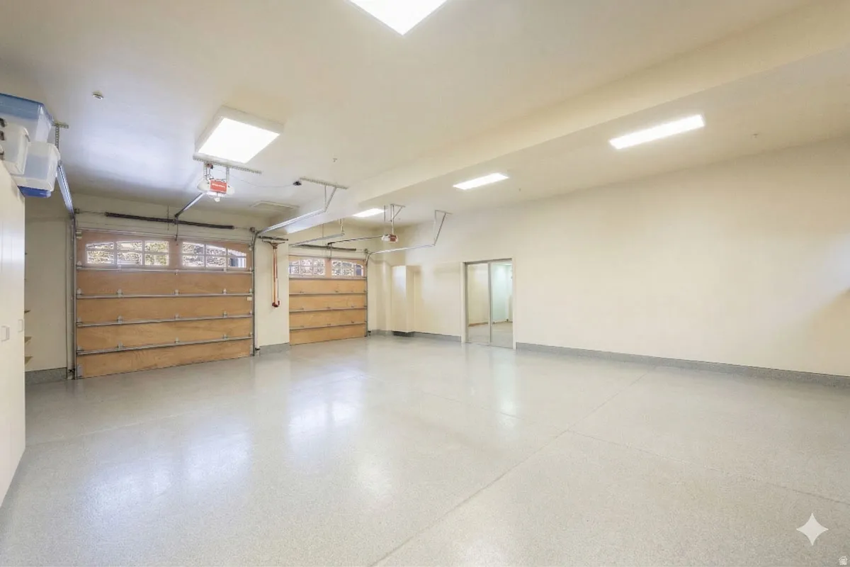 Spacious garage featuring two wood-panel garage doors with upper window inserts, an epoxy-coated concrete floor, and multiple overhead fluorescent light fixtures