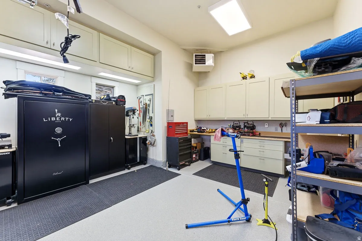 Spacious garage featuring extensive built-in cabinetry, durable epoxy flooring, overhead fluorescent lighting, and a wall-mounted heating unit