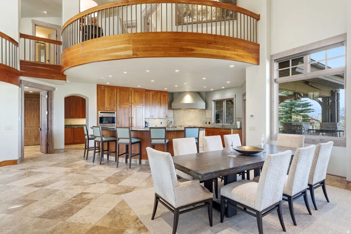 Open-concept living space featuring high ceilings, a prominent curved wood balcony with metal railings, and a large dining area with natural light