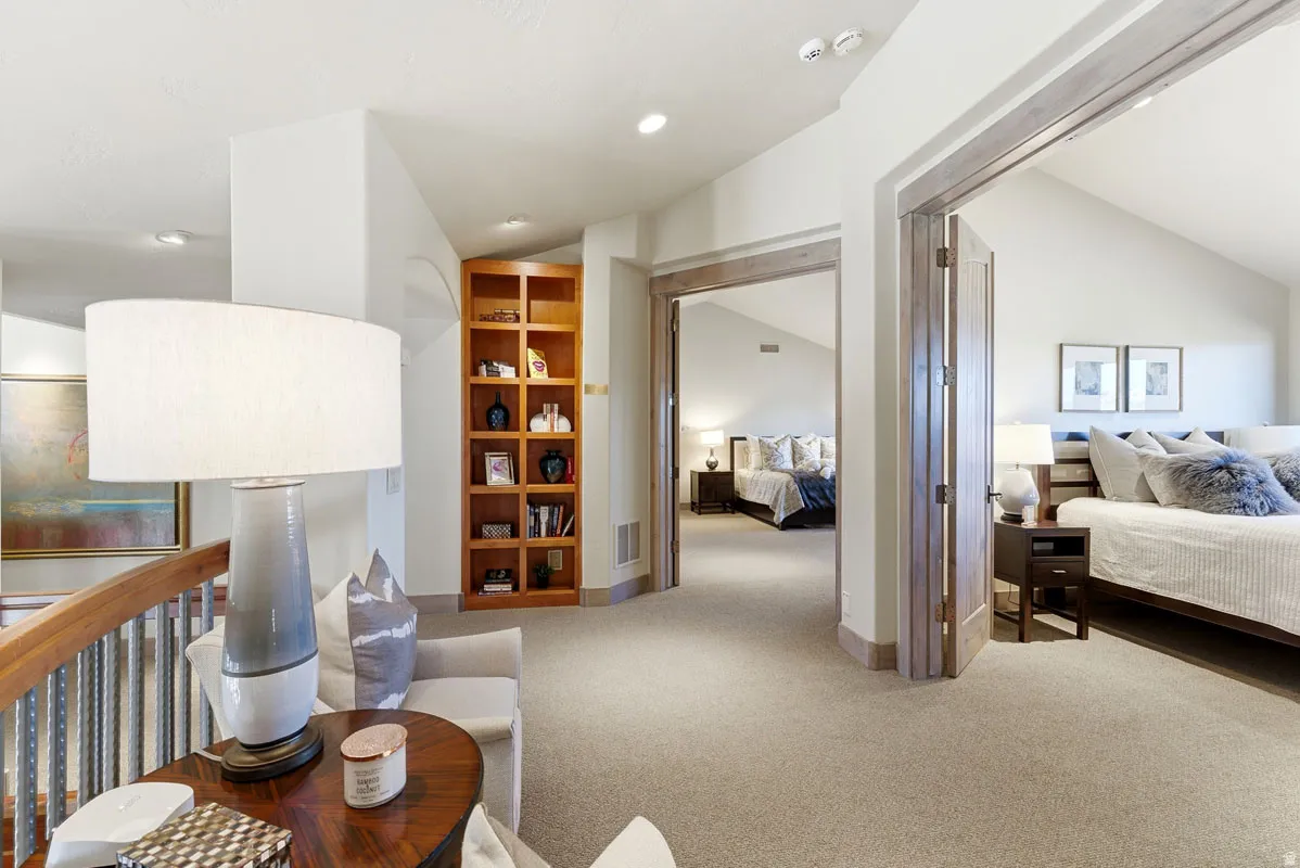 Upper-level hallway featuring a built-in wood bookshelf, wood-finished railing with dark metal spindles, and light neutral carpeting