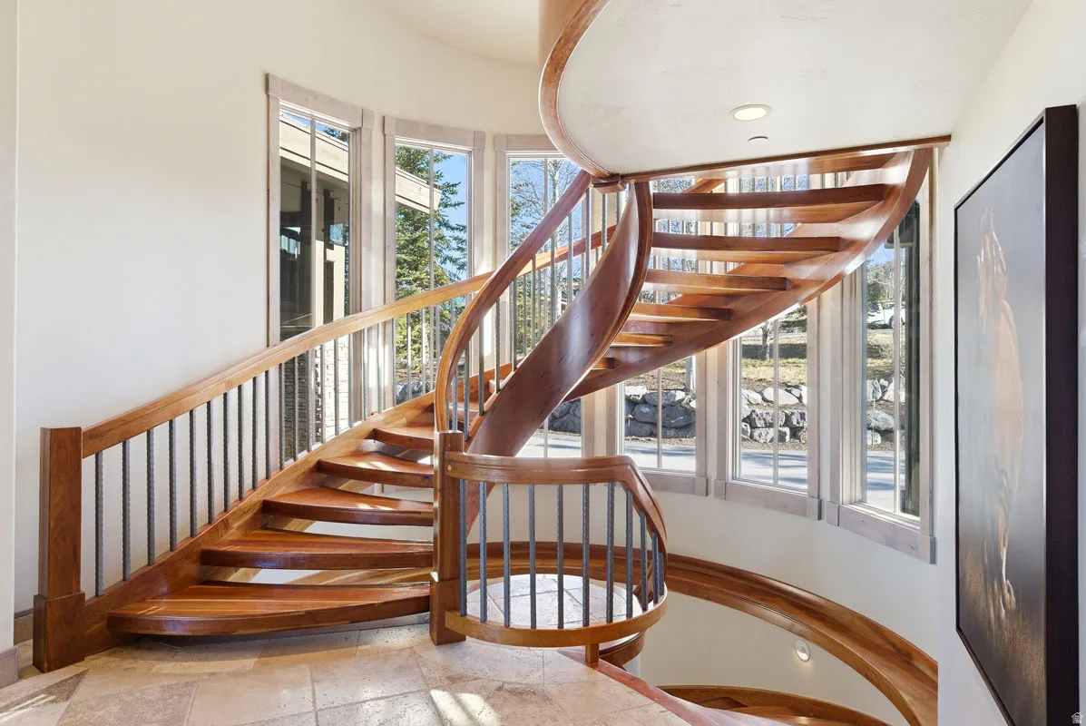 Curved wood staircase with wrought iron balusters, natural light from multiple windows, and recessed ceiling lighting