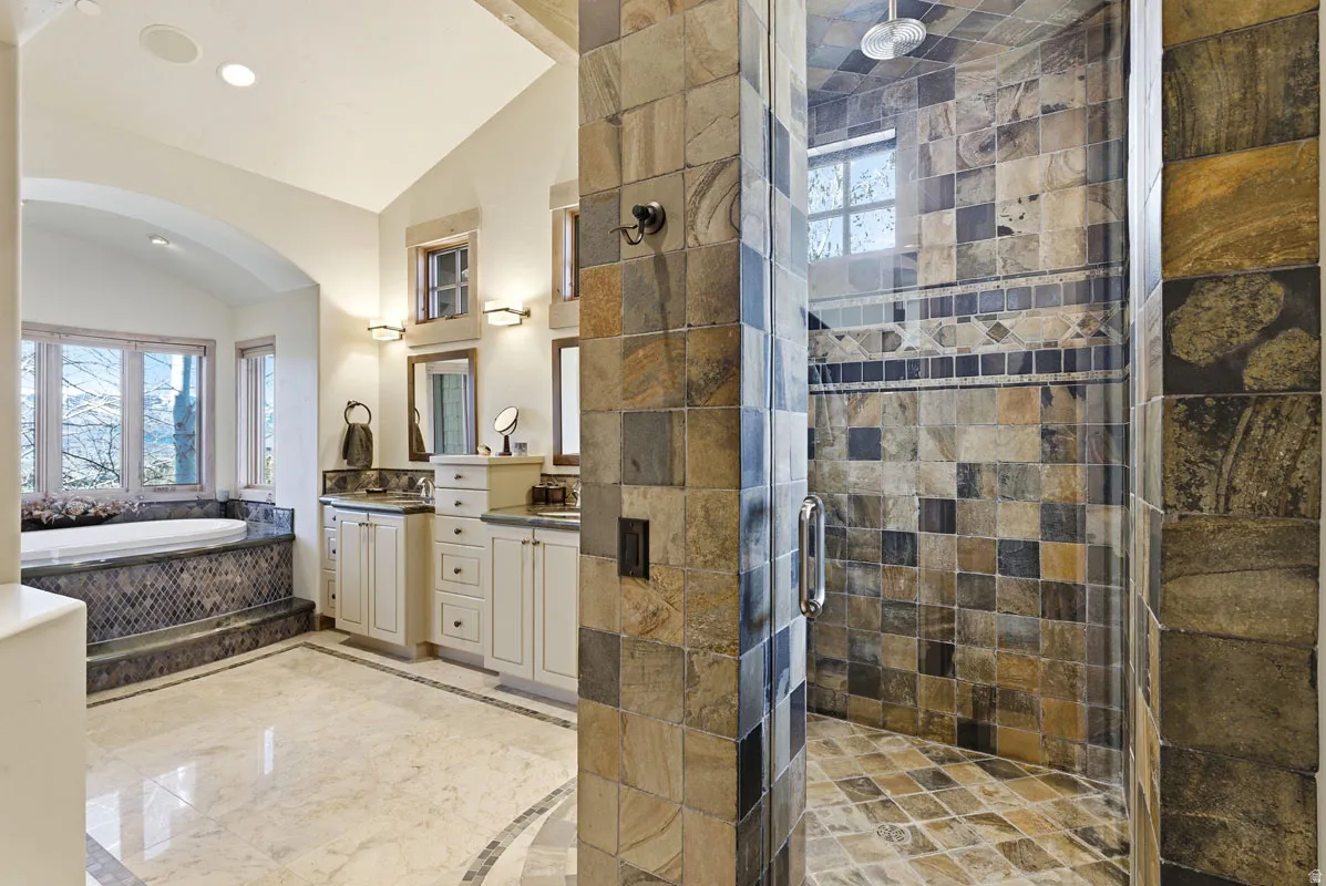 Stone-tiled walk-in shower with glass enclosure and overhead shower fixture