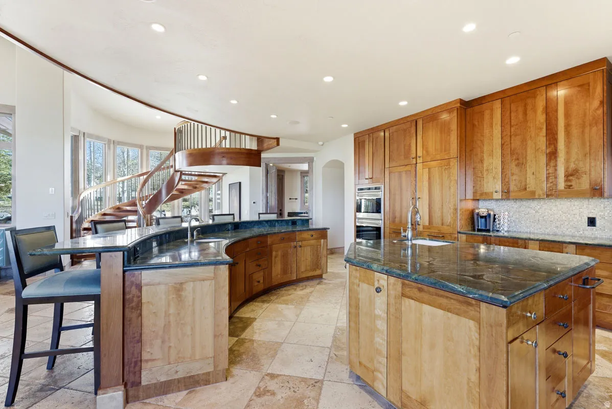 Gourmet kitchen featuring a large central island, curved breakfast bar, built-in double oven, and rich wood cabinetry with extensive storage