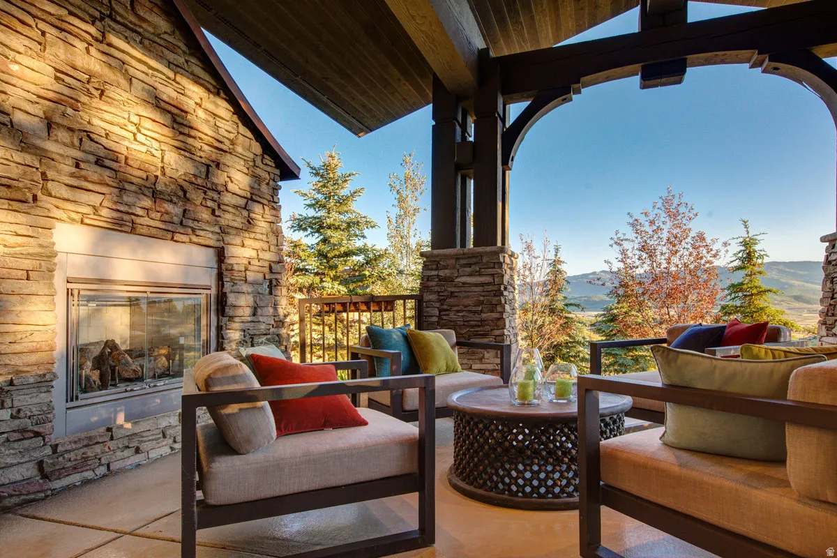 Covered outdoor patio featuring a stone-clad fireplace and wood-beamed ceiling