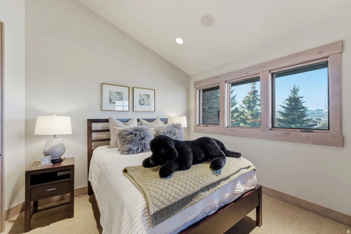 Bedroom featuring a vaulted ceiling with recessed lighting, a triple window set with natural wood trim, and wall-to-wall carpeting