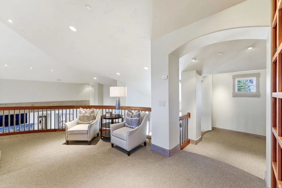 Open loft area featuring recessed lighting, a wood and iron railing, an arched entryway, and a window with wood trim