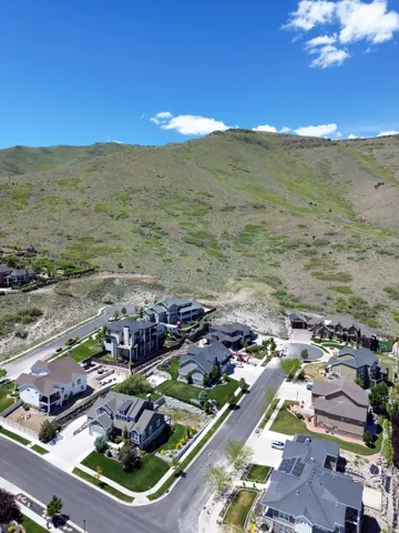 Residential community featuring paved streets and manicured lawns, bordered by natural hillside terrain