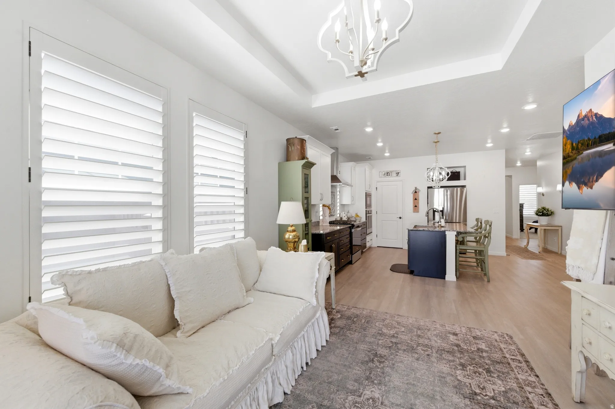 Open-concept living area featuring light wood-finish flooring, white walls, and a tray ceiling with recessed lighting