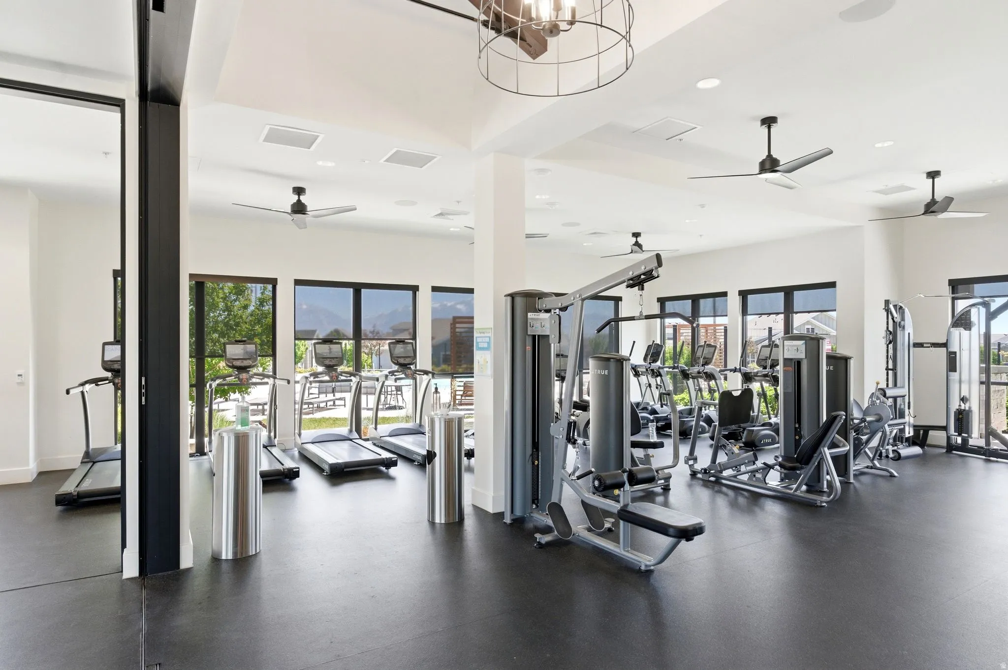 Dedicated fitness center featuring modern exercise equipment, black rubber flooring, large windows with exterior views, integrated ceiling lighting, and multiple ceiling fans