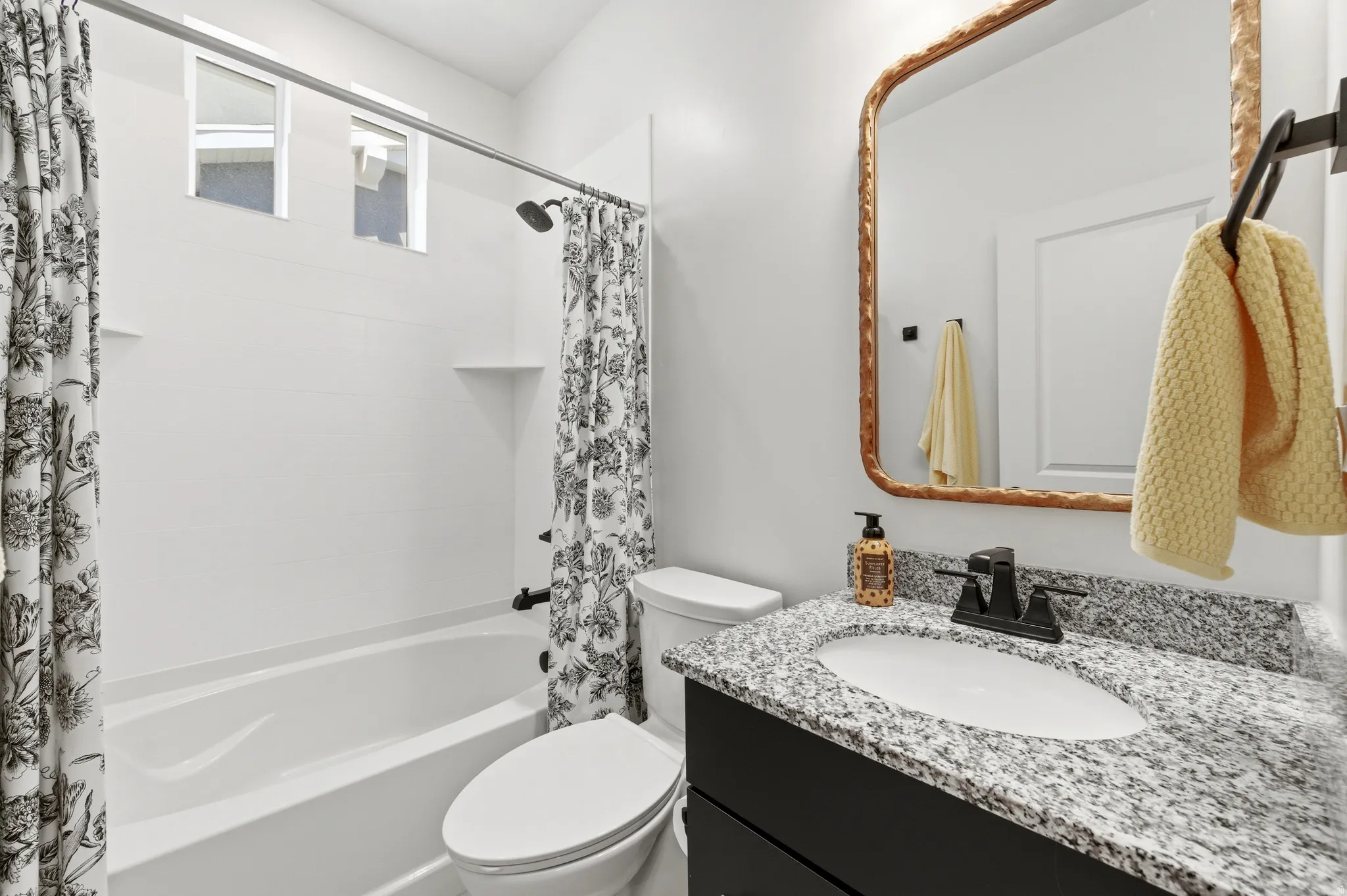 Bathroom featuring a dark vanity with a light granite countertop, white porcelain sink, and black faucet