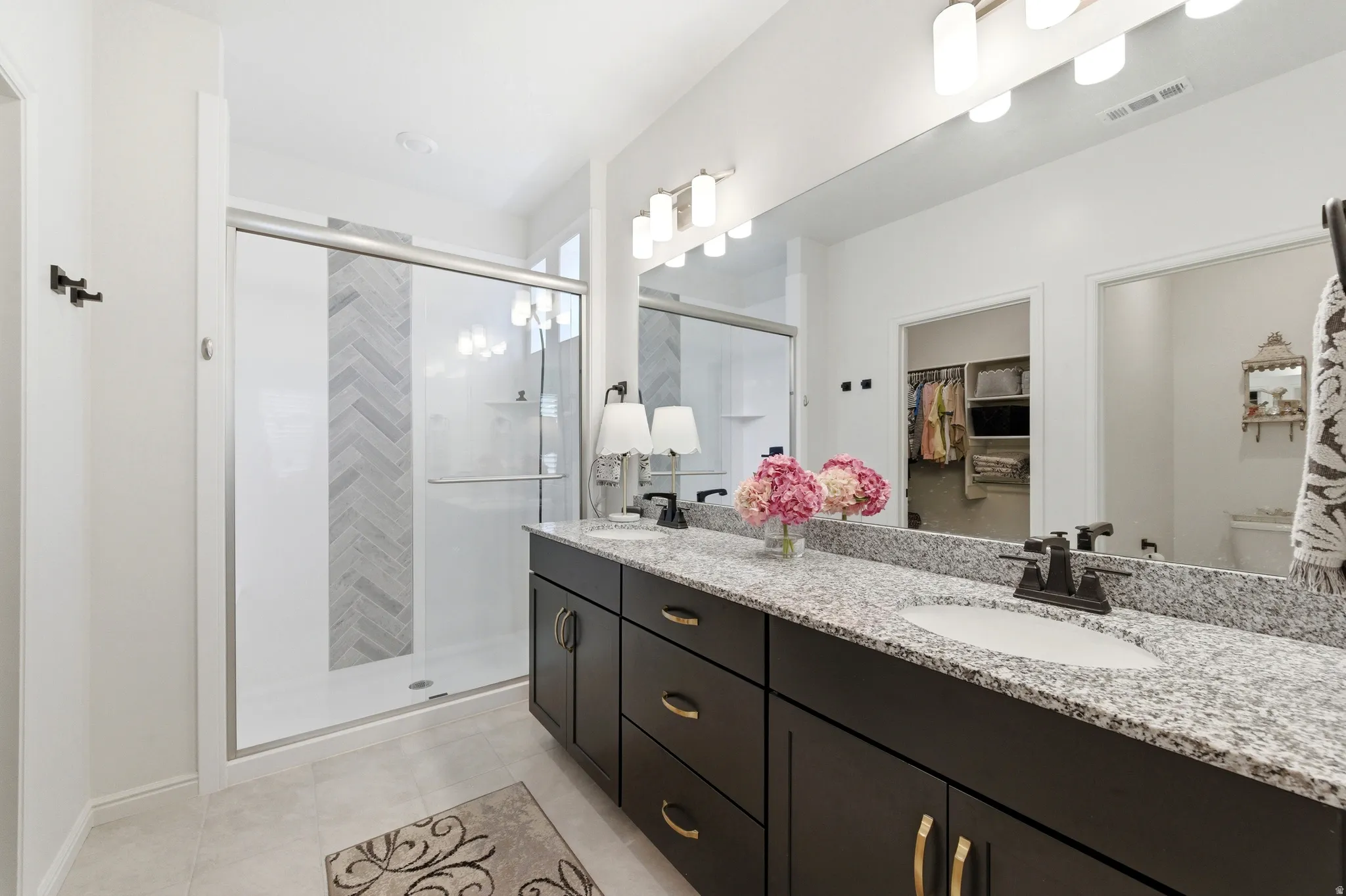 Bathroom featuring a dual vanity with a speckled countertop, undermount sinks, and dark wood cabinetry