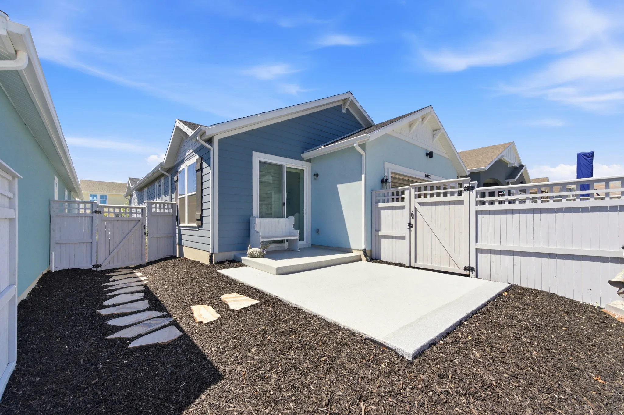 Fenced outdoor patio area featuring a concrete pad, dark ground cover, and stepping stones