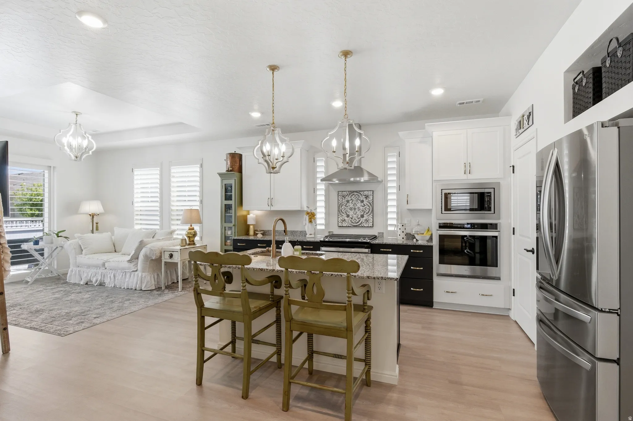 Open-concept kitchen and living area featuring light wood-finish flooring, white cabinetry, stainless steel appliances, a kitchen island with granite countertops, and decorative pendant lighting