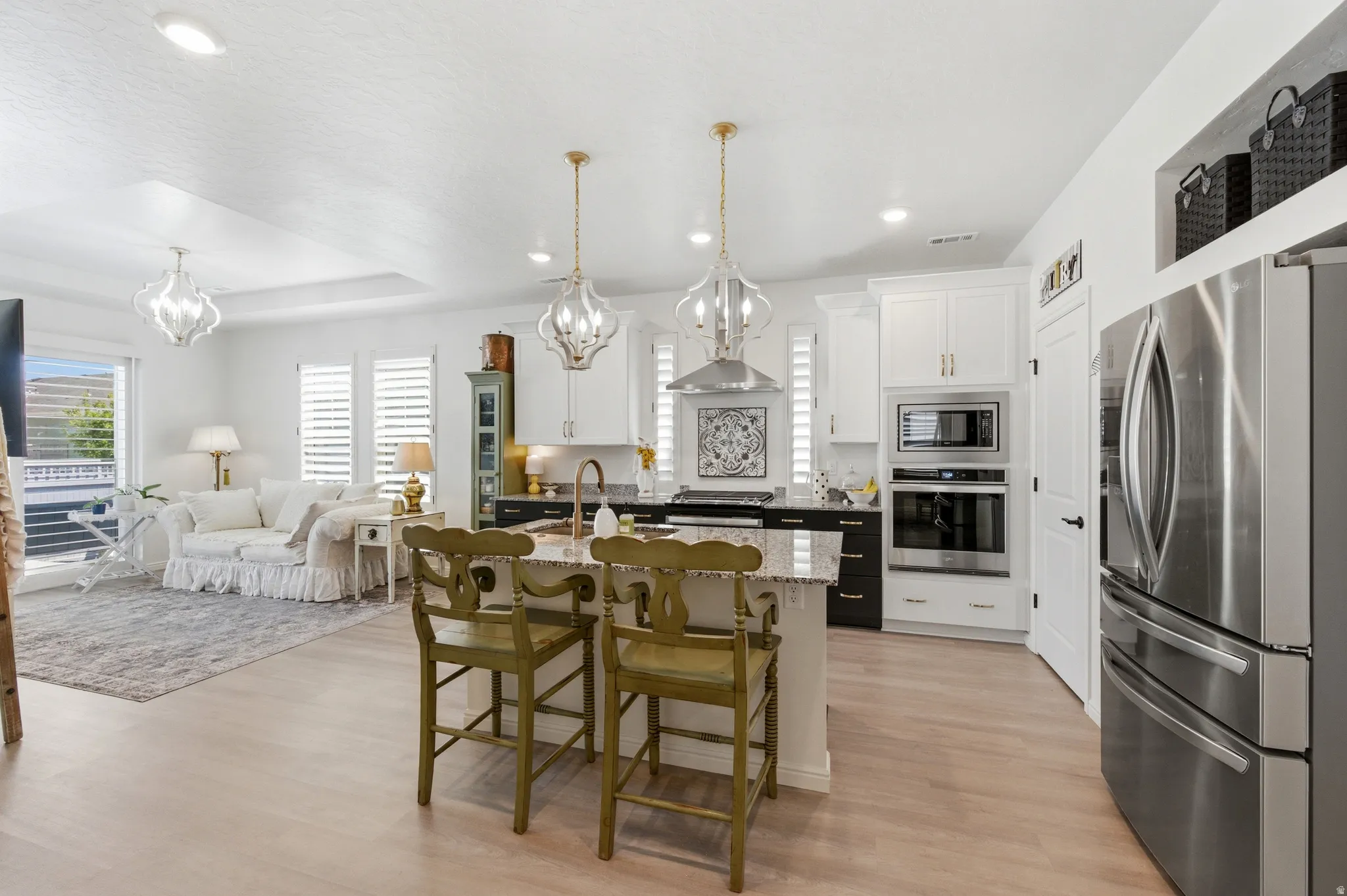 Open-concept kitchen featuring an island with seating, stainless steel appliances, white cabinetry, and granite countertops