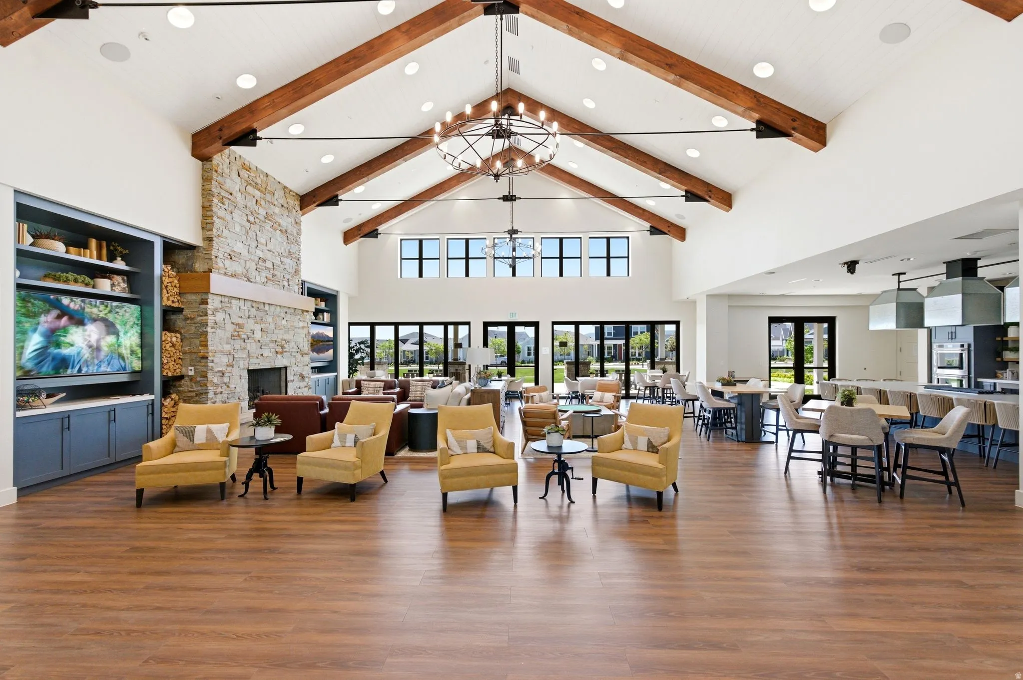 Spacious common area featuring vaulted ceilings with exposed wood beams, a stone-clad fireplace, wood-finish flooring, and expansive window walls