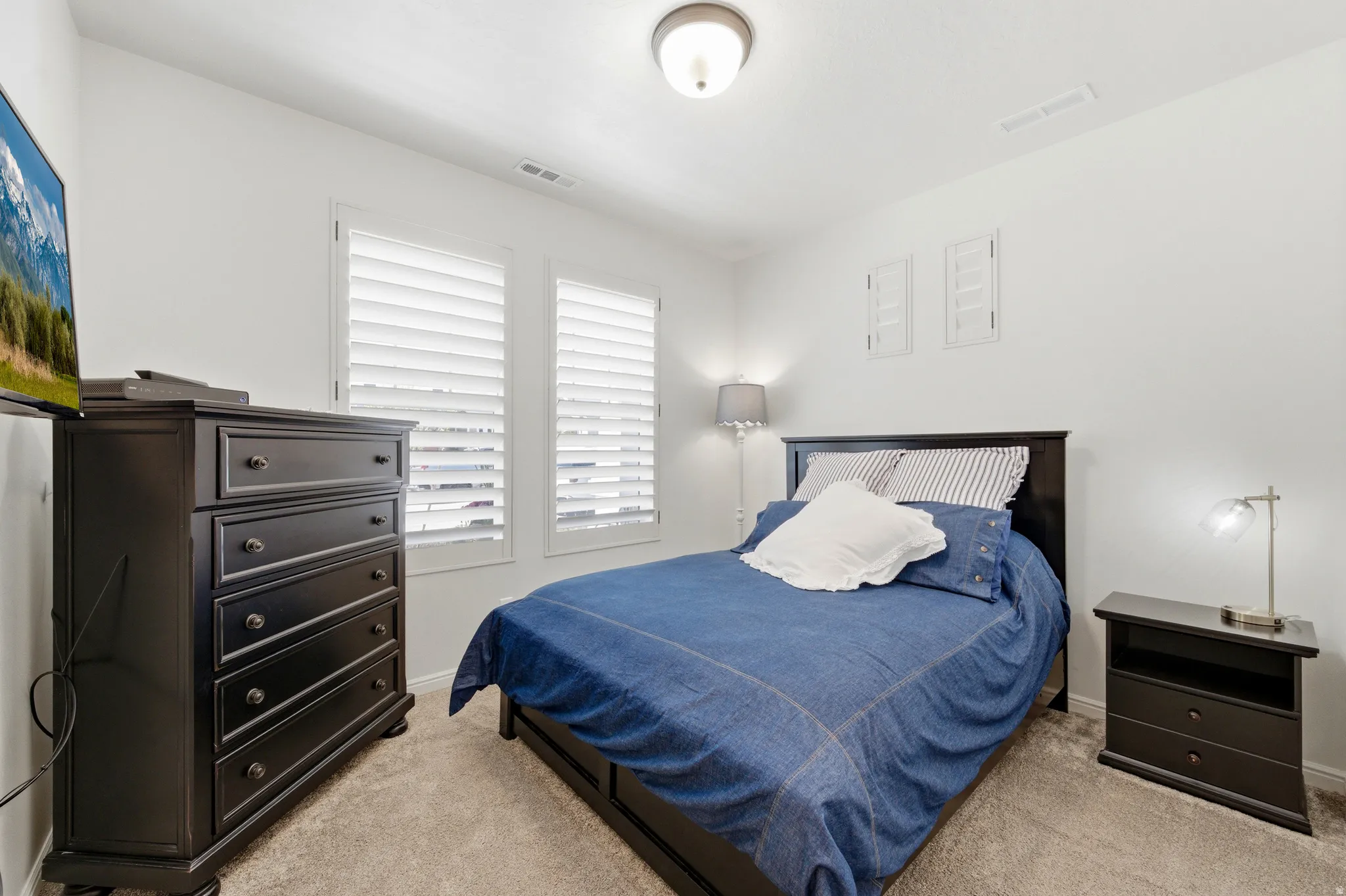 Carpeted room with white walls, two windows featuring white plantation shutters, and a flush-mount ceiling light fixture