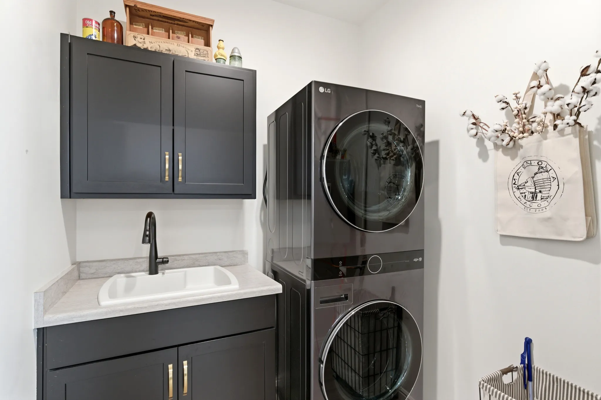 Dedicated laundry area featuring dark cabinetry with gold-toned hardware, a light-toned countertop, and an integrated utility sink with a matte black faucet