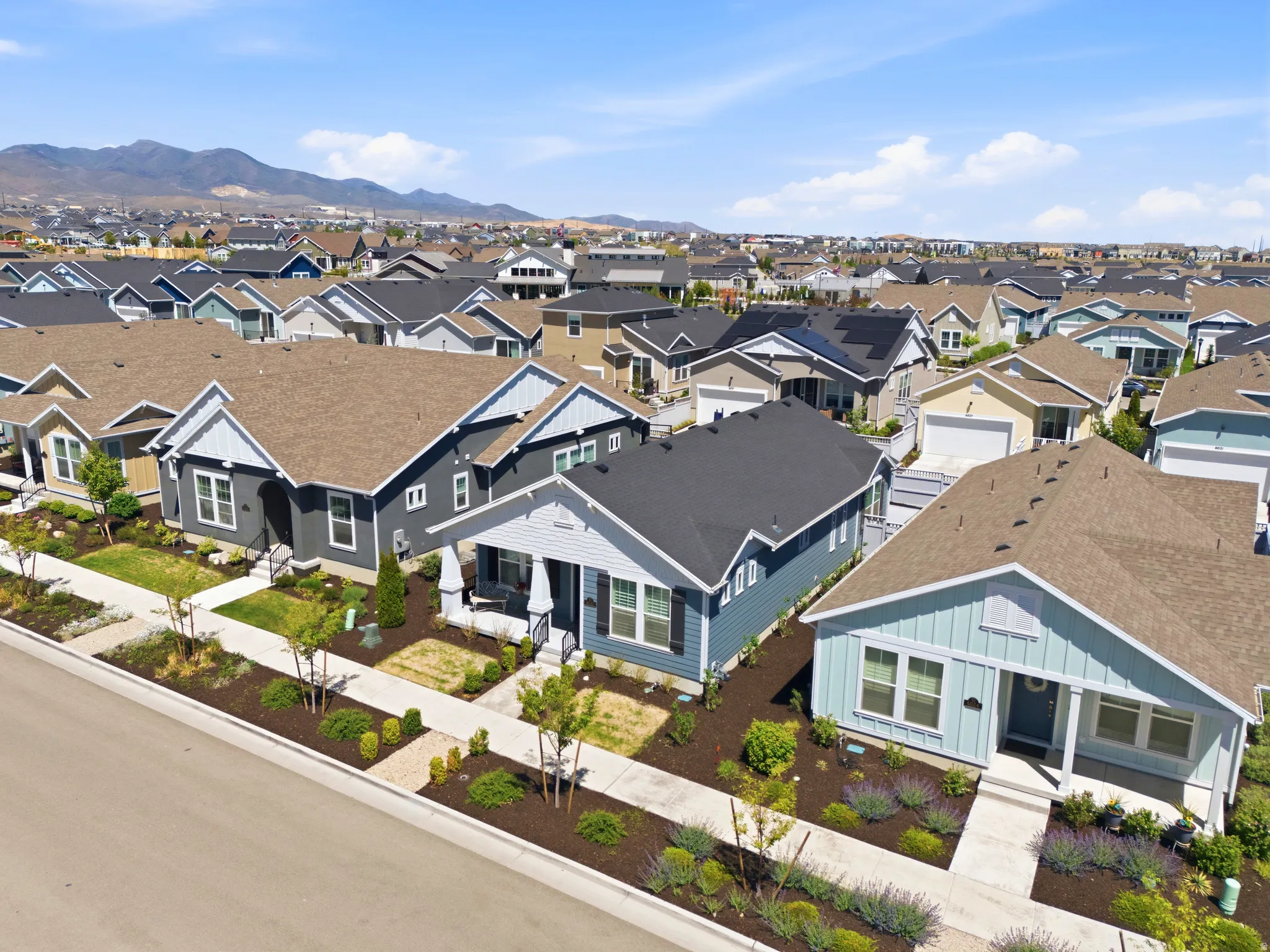 Residential streetscape featuring a row of single-story homes with varied exterior siding colors, front porches, and landscaped front yards