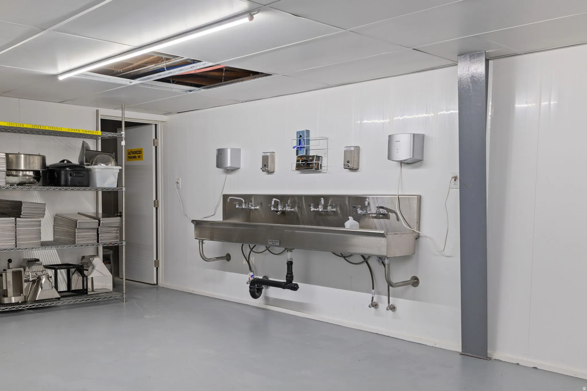 Stainless steel multi-station sink with wall-mounted soap and paper towel dispensers