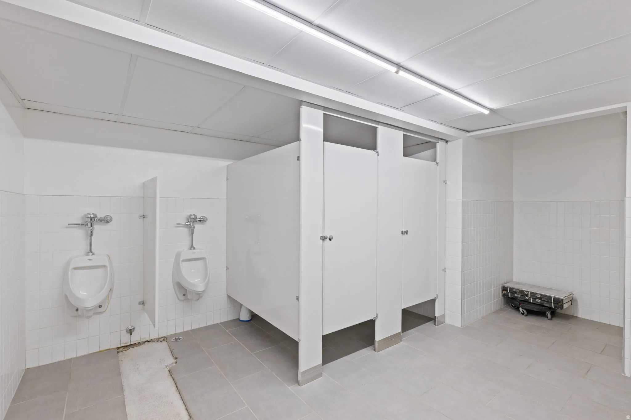 Public restroom facility featuring tiled walls, light-colored floor tiles, and ceiling-mounted linear lighting