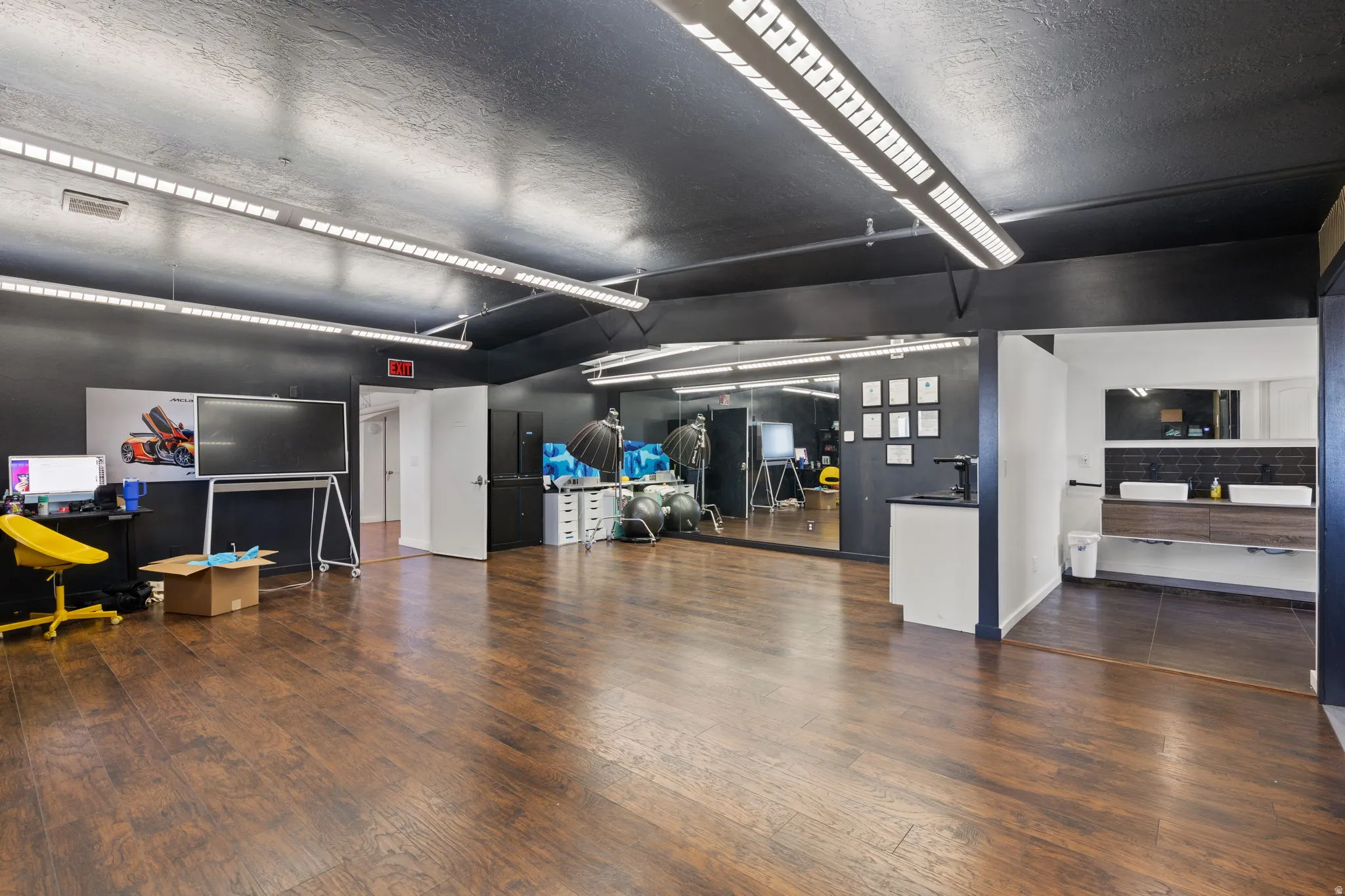 Spacious room featuring dark wood-finish flooring, a full-wall mirror, and ample overhead strip lighting