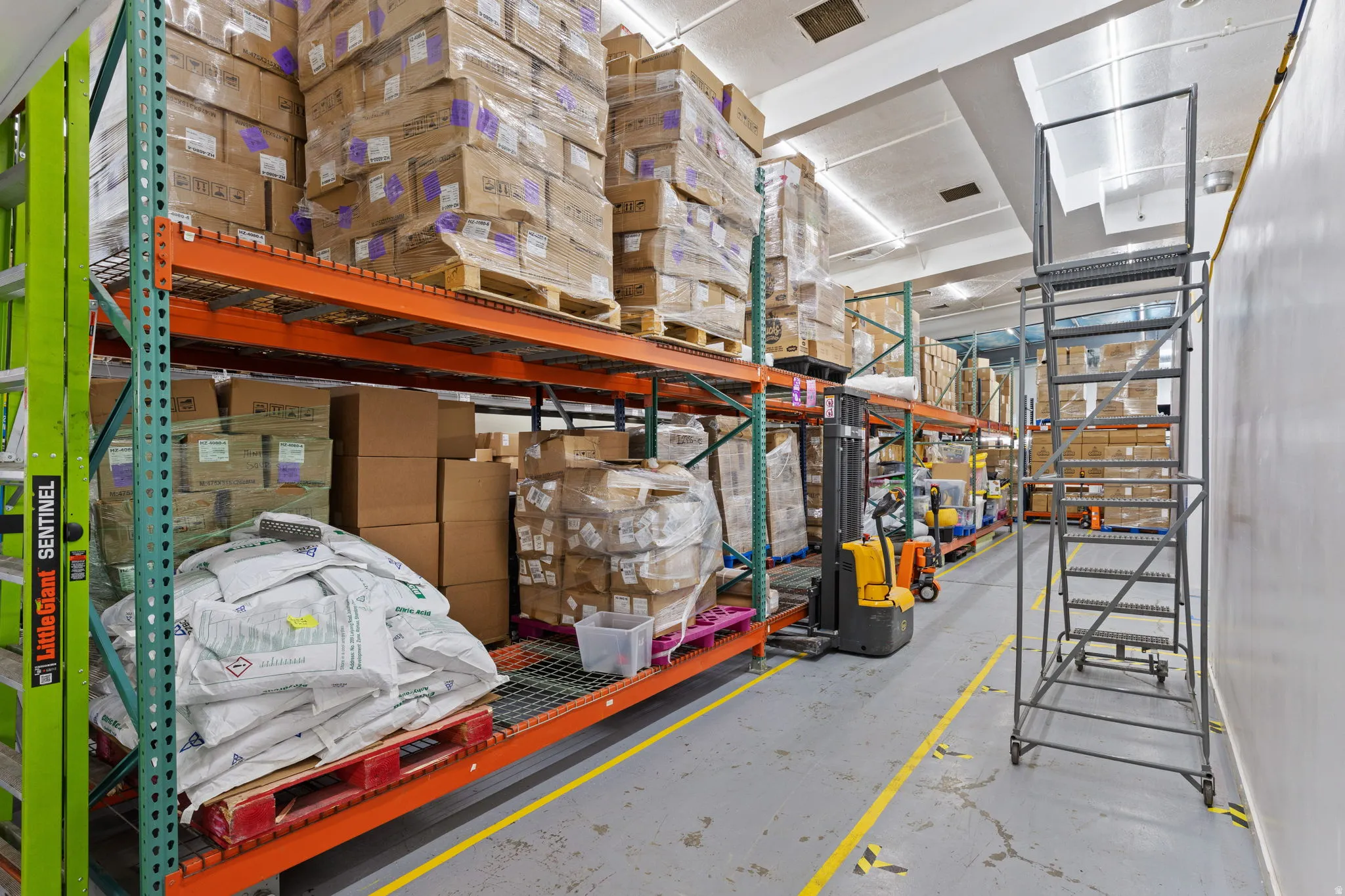 Warehouse interior with high-bay shelving, concrete flooring, and fluorescent lighting