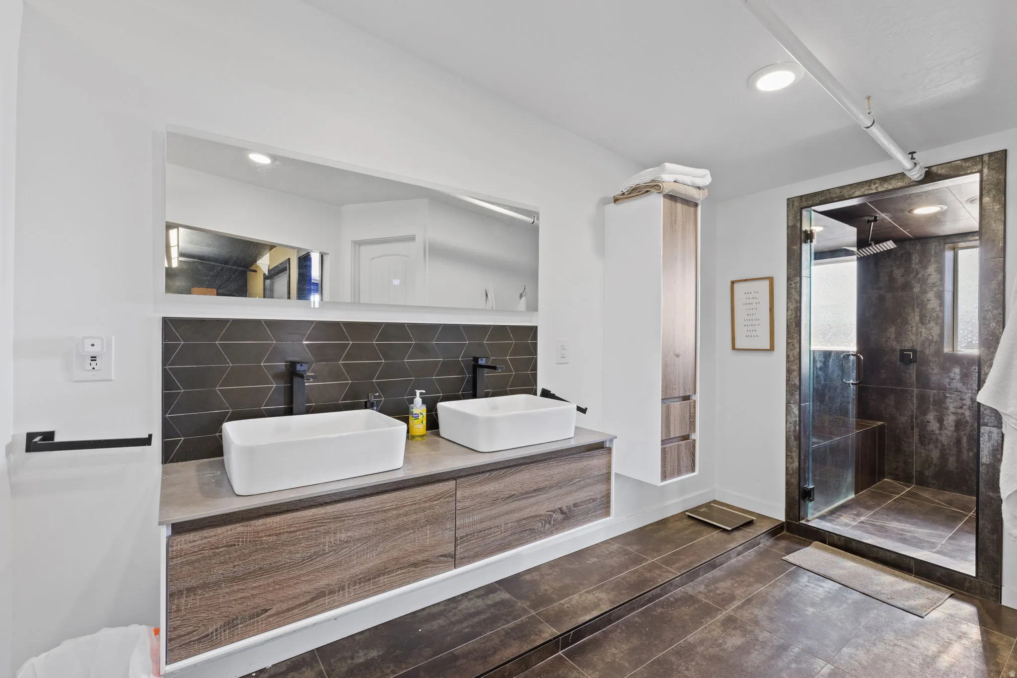 Contemporary bathroom featuring a floating dual vanity with vessel sinks, matte black fixtures, and a geometric tile backsplash