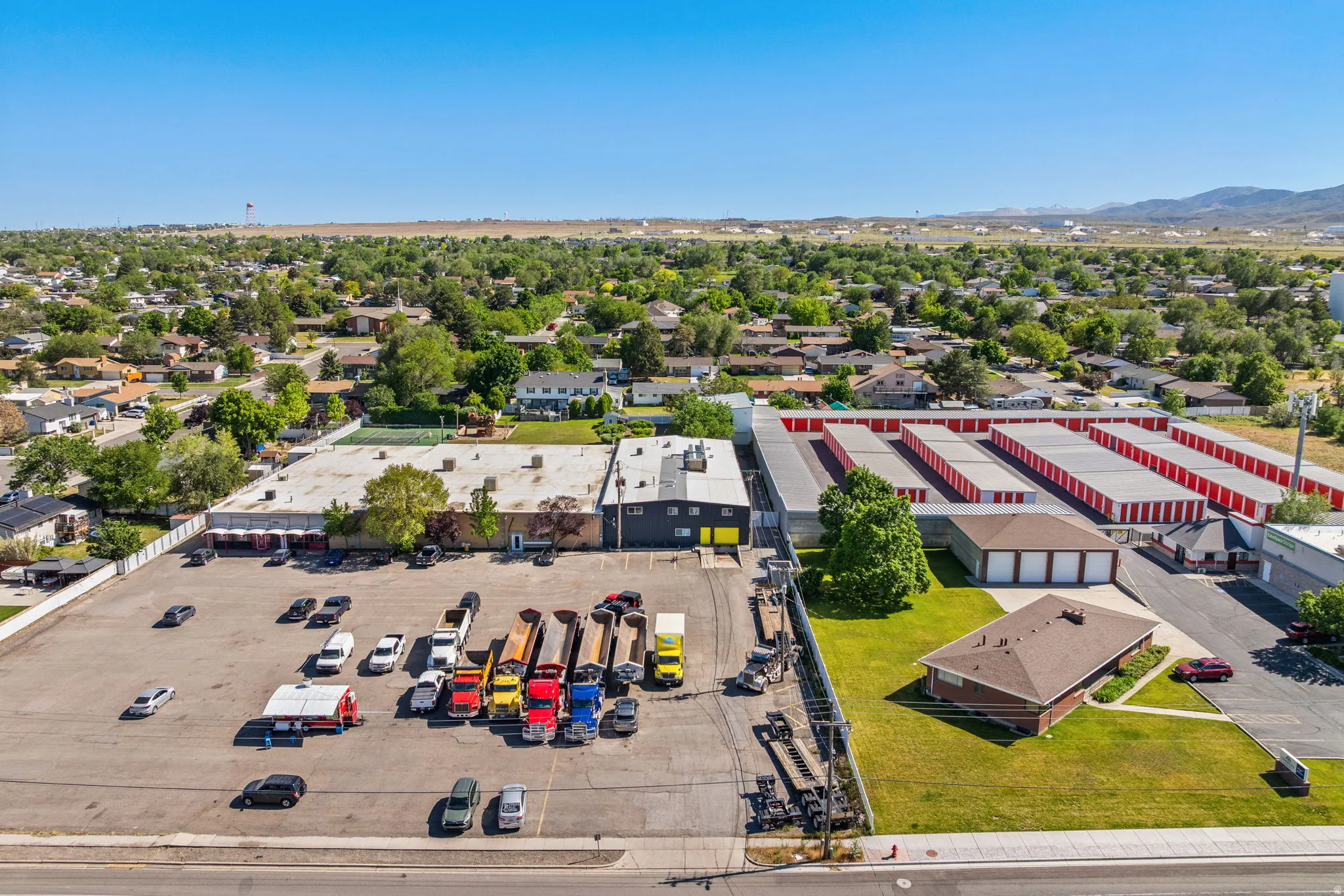 Expansive commercial property featuring multiple buildings, a large paved parking area, and an adjacent self-storage facility with red roll-up doors