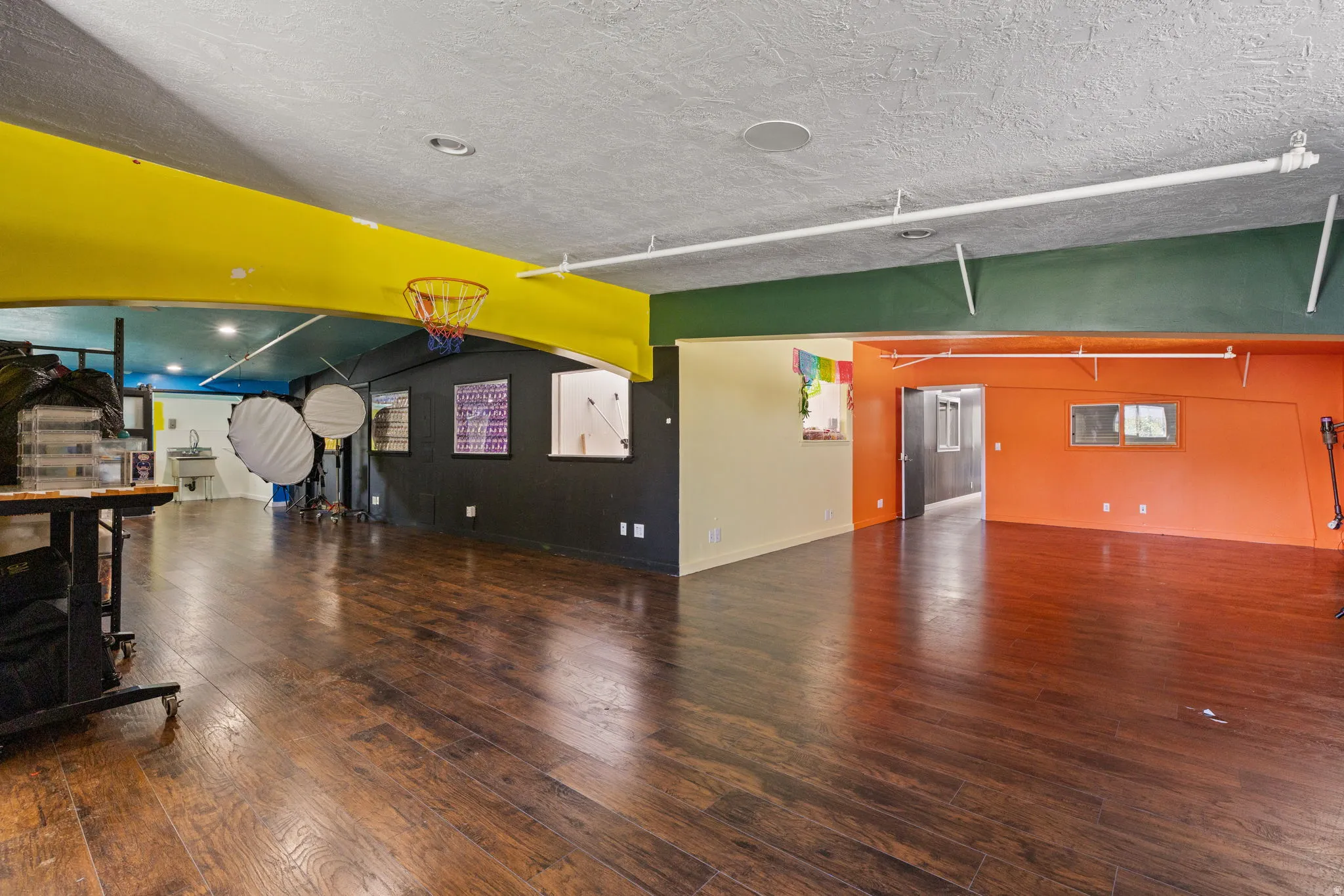 Expansive open-concept room featuring wood-finish flooring, exposed ceiling beams, and bright accent walls