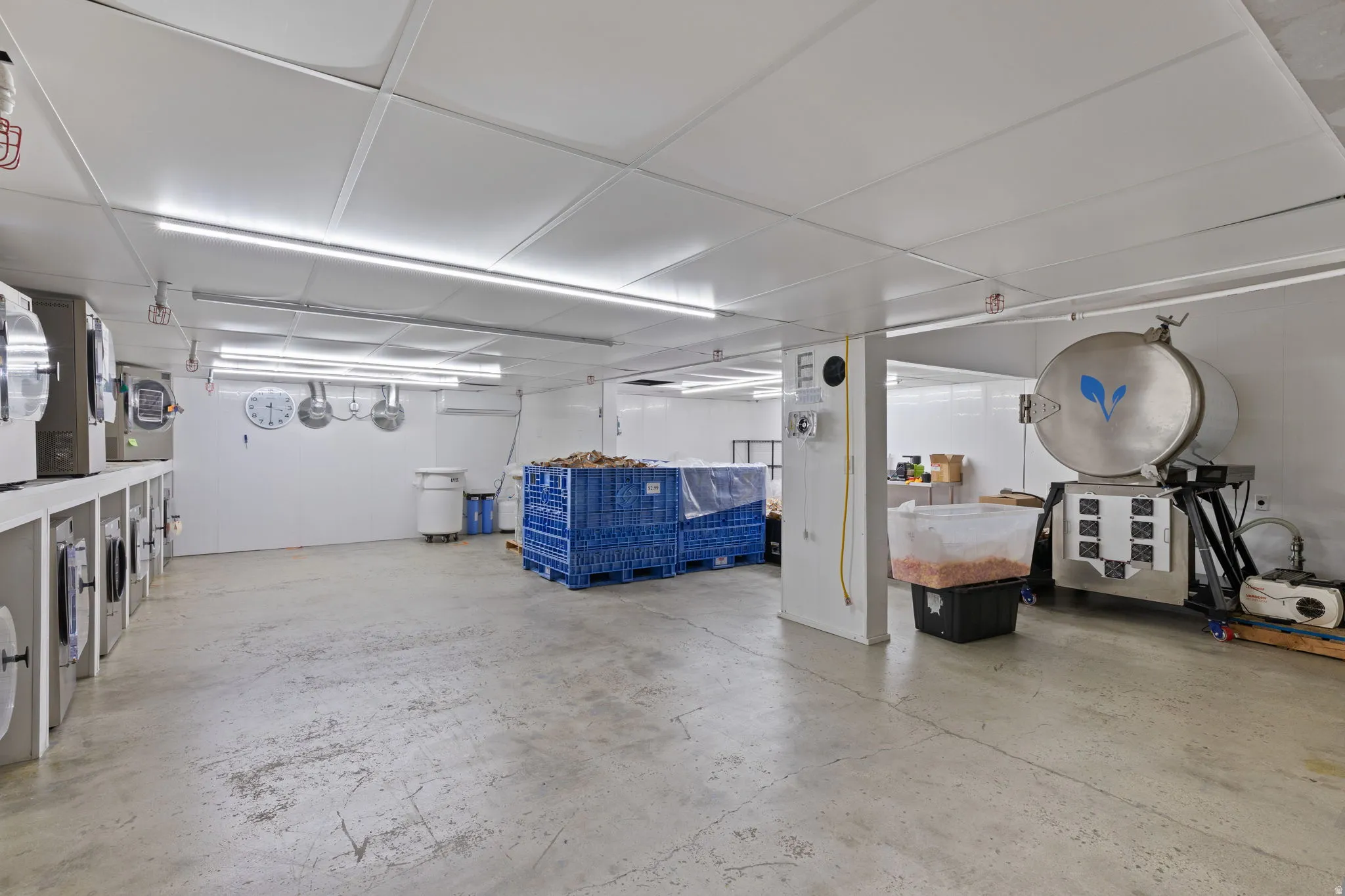 Spacious industrial interior featuring a concrete floor, white panel walls, and a white panel ceiling with integrated fluorescent lighting