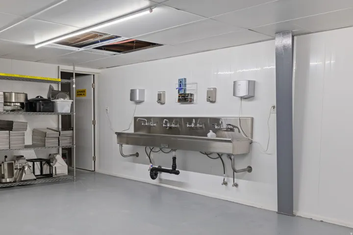 Stainless steel multi-station sink with wall-mounted soap and paper towel dispensers