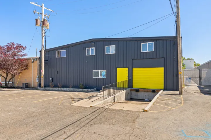 Industrial building featuring a dark gray corrugated metal exterior, multiple windows, a bright yellow pedestrian entrance door, and a bright yellow overhead door for loading access