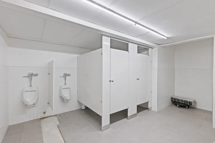 Public restroom facility featuring tiled walls, light-colored floor tiles, and ceiling-mounted linear lighting