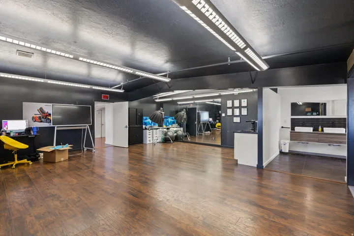 Spacious room featuring dark wood-finish flooring, a full-wall mirror, and ample overhead strip lighting