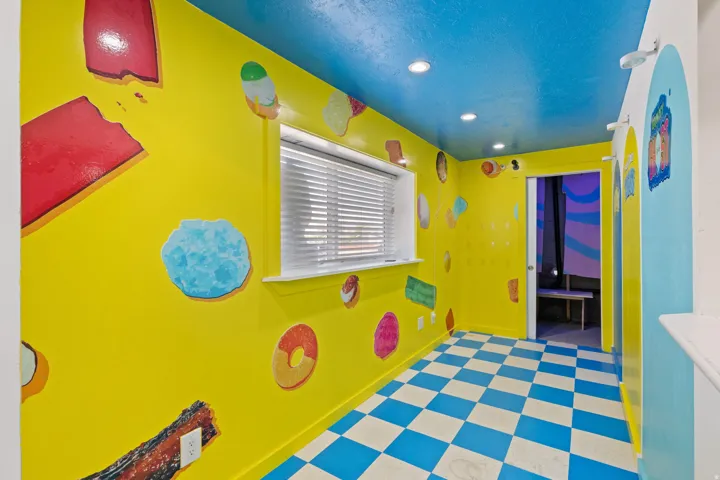 Vibrant interior space featuring a blue and white checkered floor, yellow walls with colorful graphics, and a blue ceiling with recessed lighting