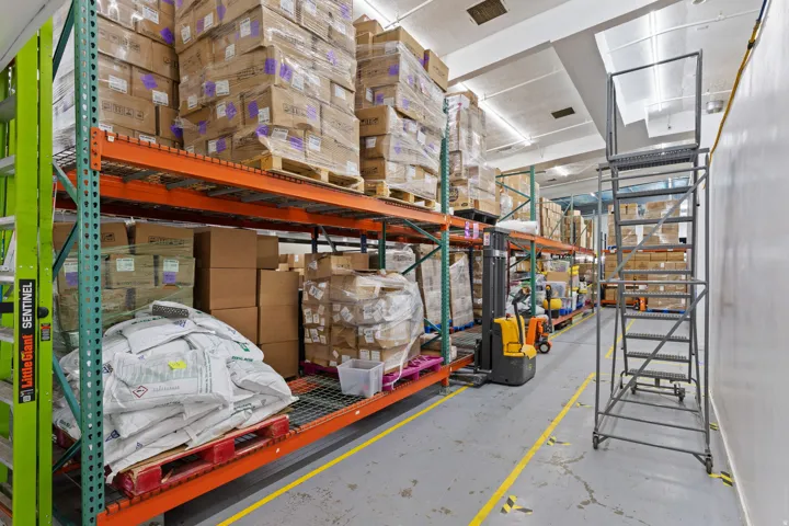 Warehouse interior with high-bay shelving, concrete flooring, and fluorescent lighting