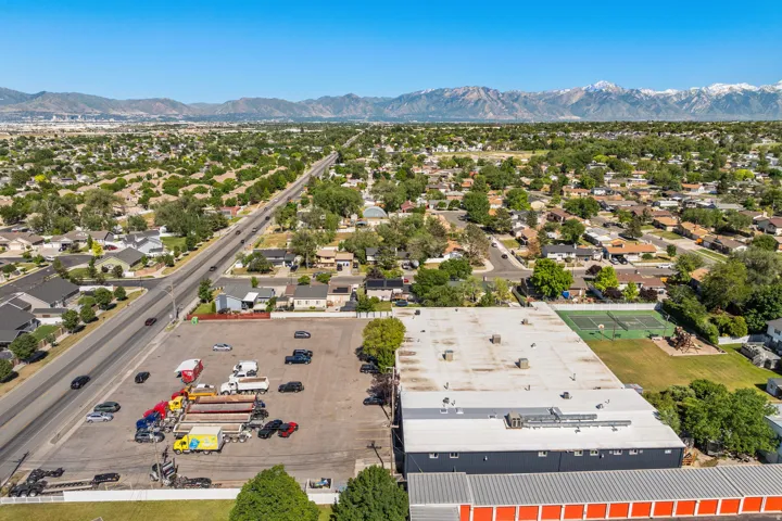 Commercial property featuring a large asphalt parking lot, an expansive industrial building with a flat roof, and an additional structure with orange-fronted storage units