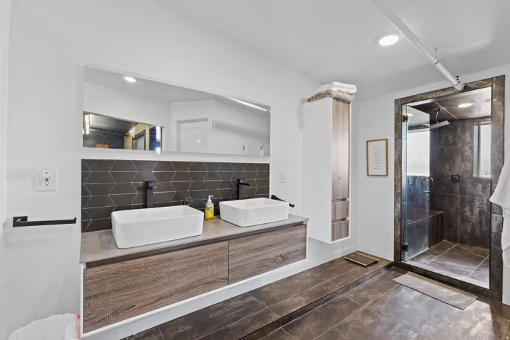 Contemporary bathroom featuring a floating dual vanity with vessel sinks, matte black fixtures, and a geometric tile backsplash