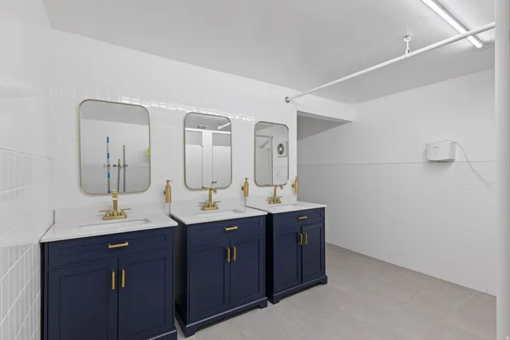 Triple vanity station featuring navy blue cabinetry, white countertops, and gold-finish fixtures