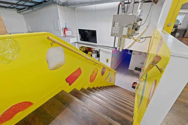 Descending wooden staircase featuring a yellow-painted banister with decorative inserts, a light wood handrail, and exposed ceiling ductwork