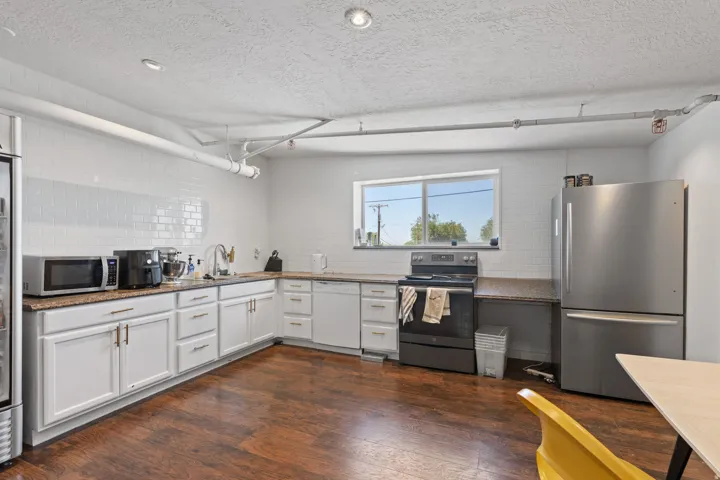 Kitchen featuring wood-finish flooring, white cabinetry with gold-tone hardware, a white subway tile backsplash, and granite-style countertops