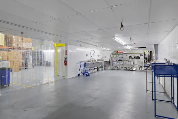 Industrial interior featuring vinyl strip curtains, drop panel ceiling, recessed lighting, and a grey epoxy floor finish