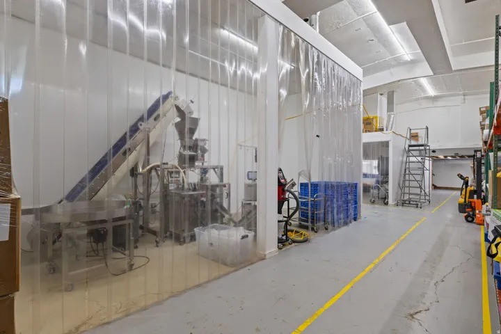 Production area featuring clear PVC strip curtains, polished concrete flooring, extensive overhead lighting, white wall panels, and high ceilings