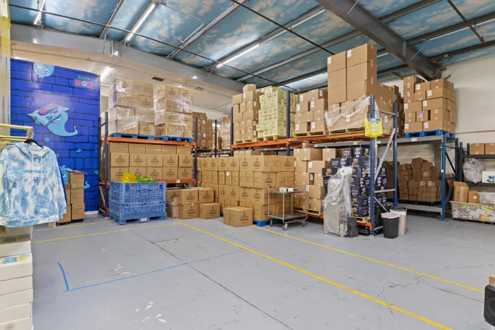 Spacious industrial interior featuring high ceilings with exposed structural beams, fluorescent lighting, and concrete flooring with yellow demarcation lines
