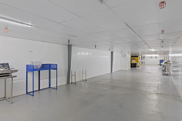 Expansive interior space featuring a light grey floor, white panel walls, and a white grid ceiling with fluorescent lighting