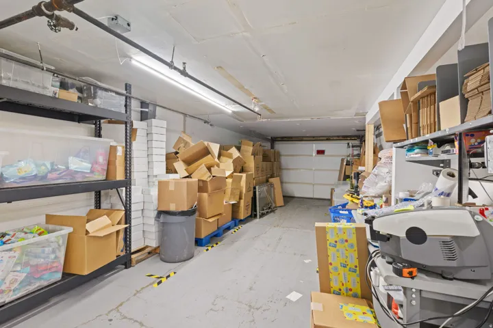 Concrete flooring with a white overhead garage door, industrial fluorescent lighting, and exposed utility piping