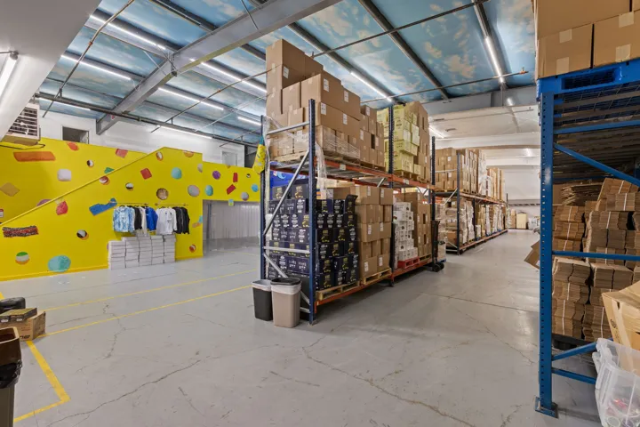 Spacious warehouse interior featuring high ceilings, exposed metal beams, and concrete flooring with yellow demarcation lines