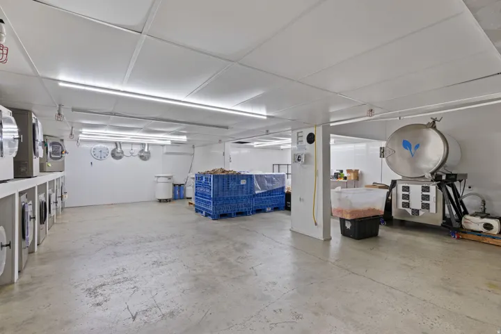 Spacious industrial interior featuring a concrete floor, white panel walls, and a white panel ceiling with integrated fluorescent lighting