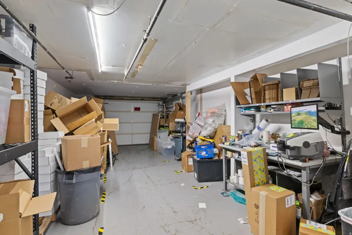 Concrete flooring with a white overhead garage door and exposed ceiling conduit