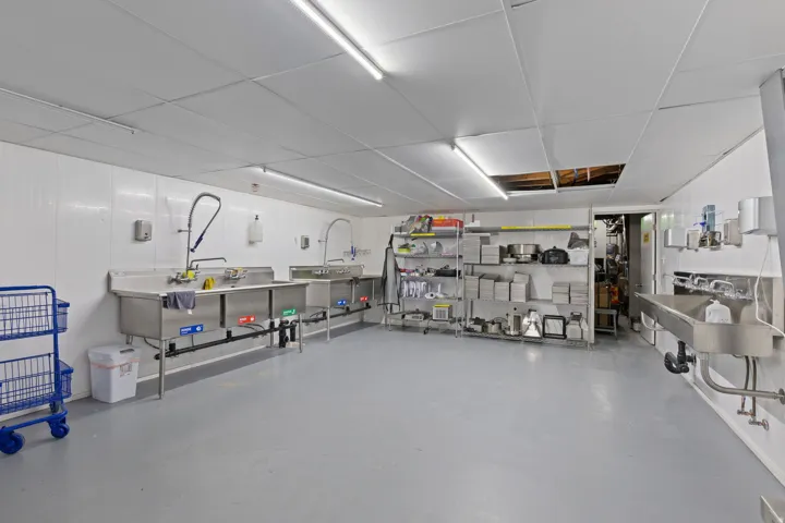 Commercial-grade kitchen area featuring stainless steel sinks, industrial wall-mounted faucets, and ample preparation space